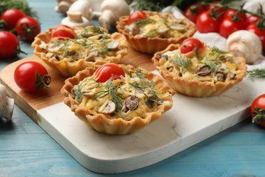 Peynirli, domatesli, mantarlı ve turkuaz ahşap masadaki dereotlu tartlar.