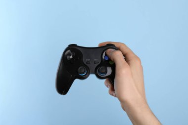 Açık mavi arkaplanda kablosuz oyun denetleyici kullanan adam, yakın plan