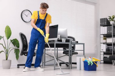 Temizlik işçisi ofiste paspas ve malzeme kovasıyla yerleri yıkıyor.