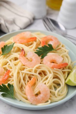 Tasty spaghetti with shrimps, lime and parsley on table, closeup