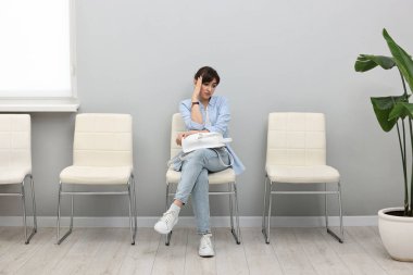 Kadın sandalyede oturuyor ve içeride randevu bekliyor.