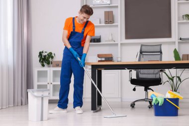 Temizlik işçisi yerleri paspasla yıkıyor. Ofiste içi malzeme dolu bir kova.