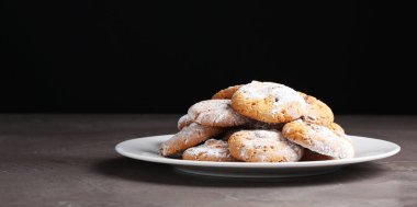 Gri desenli masadaki kurabiyelerin üzerine elek serpiştirilmiş şeker serpiştiren kadın, yakın plan.