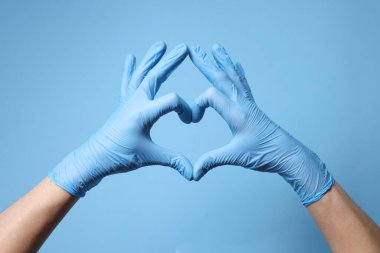 Tıbbi eldiven giyen doktor açık mavi arka planda kalp hareketi yapıyor, yakın plan.