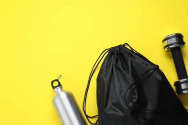 Siyah ip torbası, termik şişe ve sarı arka planda dambıl, düz konum. Metin için boşluk
