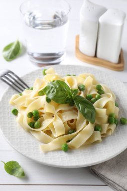 Delicious pasta with green peas served on white wooden table