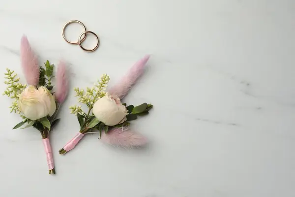stock image Small stylish boutonnieres and rings on white marble table, flat lay. Space for text