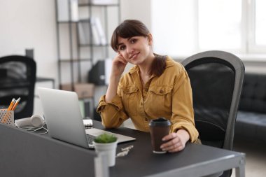 Woman with cup of coffee watching webinar at table in office