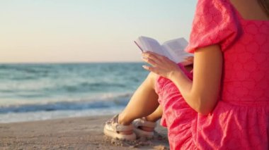 Güneşli bir sabahta deniz kenarında kitap okuyan kadın, yakın çekim.
