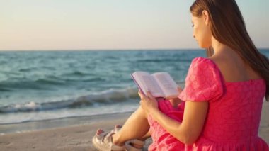 Güneşli bir sabahta deniz kenarında kitap okuyan güzel bir kadın. Kamera aşağı iniyor