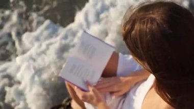 Sahilde deniz kenarında kitap okuyan bir kadın.