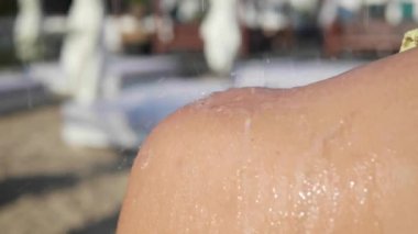 Bir kadın tatil köyünde açık havada duş alıyor, yakın plan. Kamera yukarı hareket ediyor