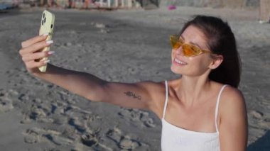 Parlak güneş gözlüklü güzel bir kadın sahilde selfie çekiyor. Kamera sağa hareket ediyor