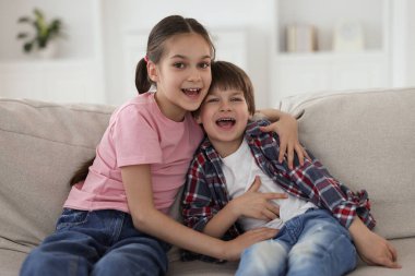 Mutlu erkek ve kız kardeşler evdeki kanepede birlikte vakit geçiriyorlar.