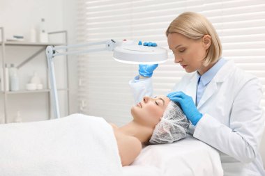 Dermatolog klinikte fener altında hastanın yüzünü inceliyor.