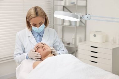 Dermatolog klinikte fener altında hastanın yüzünü inceliyor.