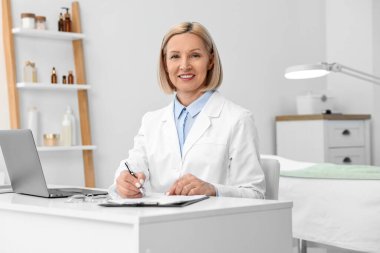 Klinikteki beyaz masada kalemle mutlu bir cildiyecinin portresi.