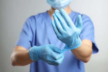 Gri arka planda açık mavi tıbbi eldiven giyen doktor, yakın plan.