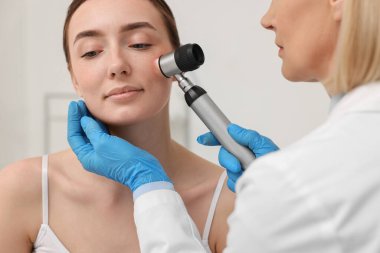 Dermatoskoplu bir dermatolog klinikte hastanın yüzünü inceliyor.