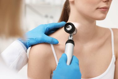 Dermatoskoplu bir dermatolog klinikteki hastayı muayene ediyor.