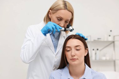 Dermatoskoplu trikoloğum klinikte hastanın saçını inceliyor.