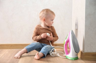 Little child playing with iron plug near electrical socket at home. Dangerous situation