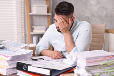 Ofisteki belgelerle çevrili bunalmış bir adam.