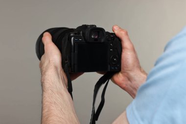 Fotoğrafçı gri arkaplanda kamera tutuyor, yakın plan.