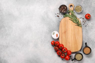 Baharat ve domateslerle çevrili tahta kesme tahtası. Gri desenli masa, düz yatak. Metin için boşluk