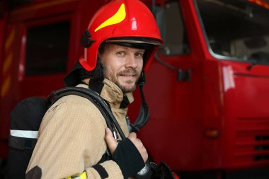 İstasyondaki kırmızı itfaiye aracının yanındaki üniformalı itfaiyecinin portresi.