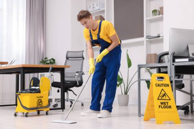 Temizlik servisi. Ofiste yerleri paspasla silen bir adam.
