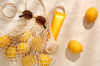 Güneş gözlüklü, limonlu, kumdaki güneş kremli bir çanta.