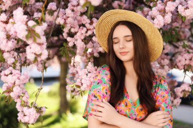 Hasır şapkalı güzel kadın bahar günü çiçek açan ağacın yanında.