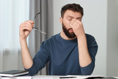 Overwhelmed man with glasses at table indoors