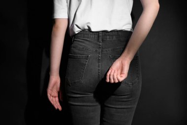 SOS gesture. Woman showing signal for help behind her back on black background, back view