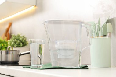 Mutfaktaki beyaz tezgahta su filtresi sürahi ve cam var.