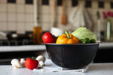 Beyaz desenli masa üzerinde farklı ıslak sebzelerle metal süzgeç.