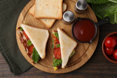 Lezzetli sandviçler, kızarmış pastırma, ketçap ve ahşap masaya baharatlar.