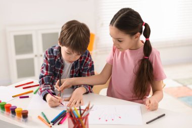 Mutlu erkek ve kız kardeş beyaz masada resim çiziyor.