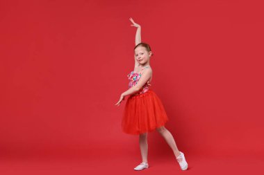 Kırmızı arka planda dans eden tatlı küçük kız.