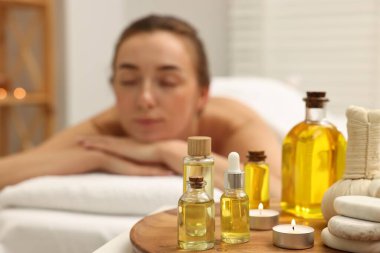 Aromaterapi. Spa salonundaki masaj koltuğunda dinlenen kadın, önemli yağ şişelerine, bitkisel poşetlere, yanan mum ve taşlara odaklan.