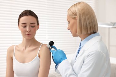 Dermatoskoplu bir dermatolog klinikteki hastayı muayene ediyor.