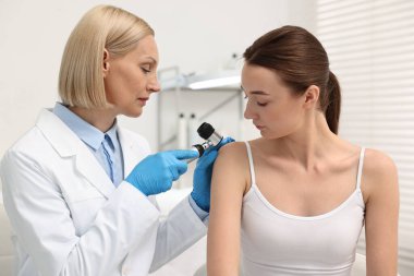 Dermatoskoplu bir dermatolog klinikteki hastayı muayene ediyor.