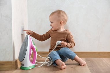 Little child playing with electrical socket and iron plug at home. Dangerous situation