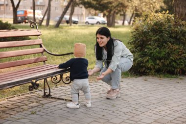 Küçük bebek parkta annesine ilk adımlarını atıyor, arkasını görüyor. Mutlu aile onu arıyor.