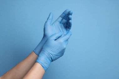 Açık mavi arka planda tıbbi eldiven giyen doktor, yakın plan.