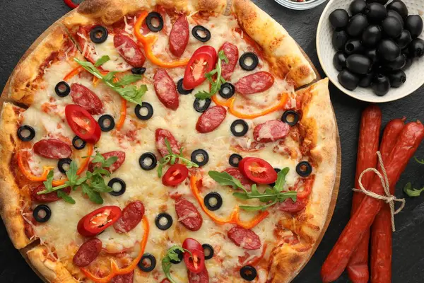 Lezzetli pizza ve malzemeler siyah masada, üst tarafta.