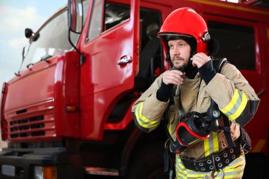 Firefighter in uniform near red fire truck at station