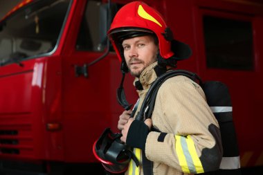 İstasyondaki kırmızı itfaiye aracının yanındaki üniformalı itfaiyecinin portresi.