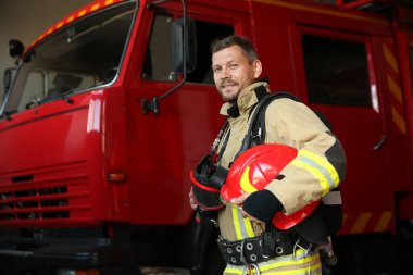 İstasyondaki kırmızı itfaiye aracının yanında miğferli itfaiyeci.